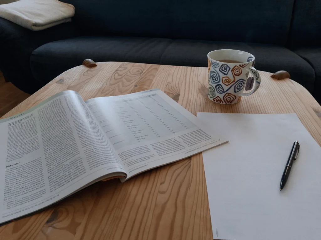 Fachzeitschrift und Notizen – fundierte Antworten auf Ihre Fragen Aufgeschlagene Fachzeitschrift mit Tabellen neben bunter Teetasse und Notizblock auf Holztisch – Symbol für fundierte Antworten bei Fragen zu Erschöpfung