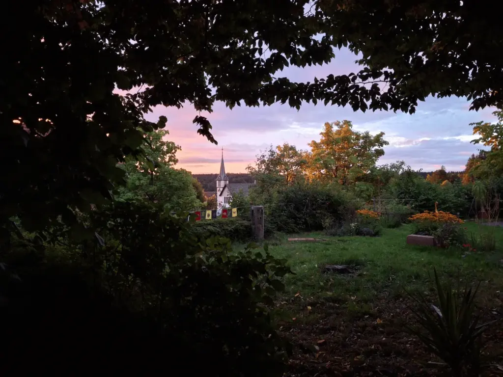 Blick über einen Garten auf die Kirche von Schernbach im Abendlicht – Zeit für sich als Angehöriger eines depressiven Partners